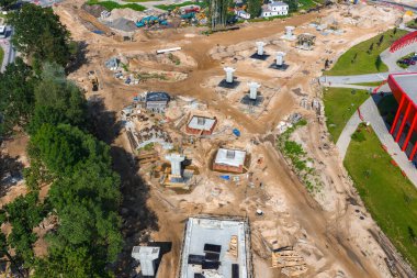 Letonya 'da Riga' dan Jelgava yoluna kadar büyük bir inşaat sahası beton sütunlar, ağır makineler, toprak yollar ve yeşillikler arasında kırmızı bir yapı..