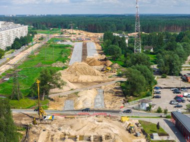 Riga 'dan Jelgava yoluna kadar geniş ölçekli yol inşaatı vinçler, kazıcılar, kum yığınları, bir iletişim kulesi, bir yerleşim kulesi ve arka planda bir orman..