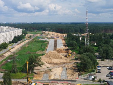Riga 'dan Jelgava yoluna kadar geniş ölçekli yol inşaatı. Kazı araçları ve vinçlerle çevrili. Konut binası, iletişim kulesi, yeşil alanlar ve orman alanı var..