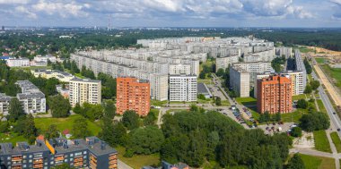 Riga, Letonya 'nın yoğun nüfuslu Ziepniekkalns semtinde turuncu ve beyaz daireler, yeşillikler, Riga TV Kulesi ve görünür bir yol şantiyesi yer alıyor..