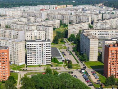 Ziepniekkalns bölgesinde çok katlı çok katlı apartmanlar, yeşil alanlar, otoparklar ve arka planda bir orman alanı var..