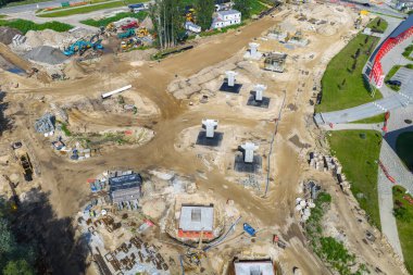 Letonya 'da Riga' dan Jelgava yoluna kadar büyük inşaat sahasında beton sütunlar, ağır makineler, çalışma alanları, yeşillikler ve yakınlardaki küçük binalar var..