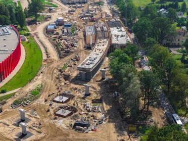 Riga 'dan Jelgava yoluna kadar geniş ölçekli yol inşaatı. Yüksek kesimler, beton sütunlar, ağır makineler ve Letonya' da yeşilliklerle çevrili kırmızı eğimli bir bina..