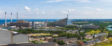 Amager Bakke 'nin yeşil alanlar, su yolları ve uzaktaki Öresund Köprüsü ile çevrili eğimli tasarımıyla enerji santraline hava görüntüsü.