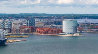 Danimarka, Kopenhag 'ın havadan görünüşü, parlak silindirik bir bina, kırmızı tuğla yapılar, kenetlenmiş bir yolcu gemisi ve su üzerinde bir köprü gösteriyor..