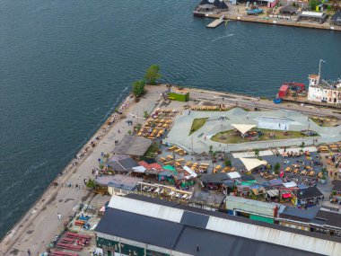 Kopenhag, Danimarka 'da bir rıhtım manzarası, Reffen gıda mahkemesi bölgesi, bir kaykay sahası, renkli koltuklar, küçük yapılar, botlar ve yakınlardaki sanayi binaları.