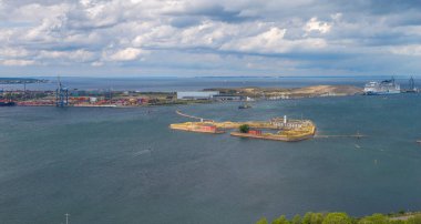 Kopenhag limanındaki Trekroner Adası 'nın havadan görüntüsü. Sarı ve kırmızı binalar, bir yolcu gemisi, endüstriyel vinçler ve bulutlu gökyüzünün altındaki mavi sular..