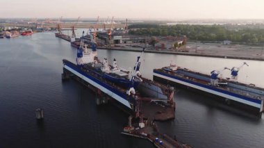 Riga, Letonya 'da bir tersane, rıhtıma yanaşmış gemilerin yanında vinçler hareket ediyor. Günbatımı, endüstriyel ortama ve sakin su yoluna ılık bir ışık saçıyor..