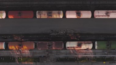 Letonya 'da gün doğumunda veya günbatımında asfalt yolda paralel giden beyaz bir kamyonla raylardaki renkli tanker vagonlarının hava perspektifi.