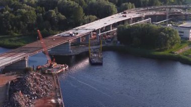 Riga, Letonya 'da kısmen tamamlanmış bir köprü, vinçler, iskeleler ve yeşil ve endüstriyel binalarla çevrili etkin yapılar ile bir su geçidi boyunca uzanır..