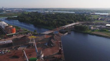 Riga, Letonya 'da köprü inşaatını, vinçleri, depoları, bacaları ve şehir simgelerini gösteren sanayi bölgesi..