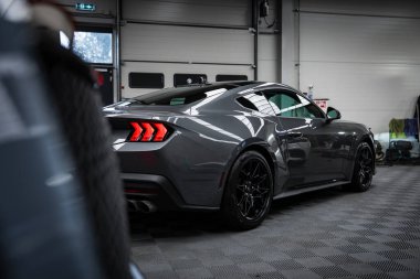 Gri Ford Mustang GT 5.0 aydınlatmalı stop lambaları, siyah alaşımlı tekerlekleri ve profesyonel bir garaj ortamında parlak bir finiş..