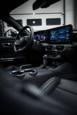 Ford Mustang GT 5.0 dahili dijital ekran, siyah deri koltuklar ve arka planda görünen kapıları olan bir garaj ayarı..