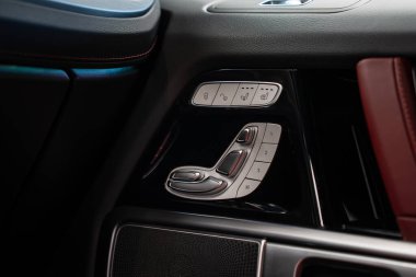 Metalik koltuk ayarlama kontrolleri, kırmızı dikişli siyah deri ve kırmızı deri kolluk içeren bir Mercedes AMG G sınıfının iç paneli..