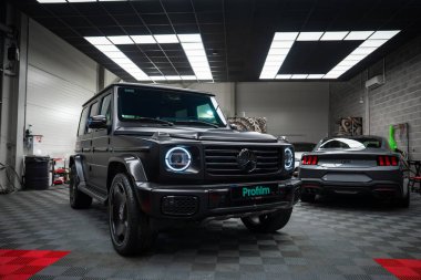 Aydınlatılmış LED farları ve gri Ford Mustang GT 5.0 'ı olan siyah bir Mercedes AMG sınıfı..