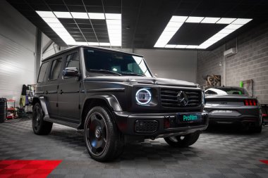 Modern bir garajda dairesel LED farları olan parlak siyah bir Mercedes AMG sınıfı. Siyah bir Ford Mustang GT 5.0 arka planda kısmen görünür.