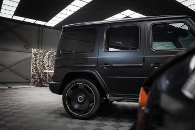 Siyah renkli camlı siyah bir Mercedes AMG sınıfı SUV ve modern ışıklandırmanın altında kapalı bir zemine park edilmiş kalın tekerlek jantları..