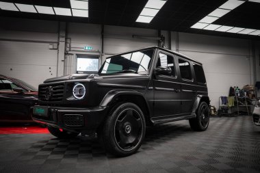 Siyah siyah bir Mercedes AMG sınıfı SUV. Dairesel LED farları içeride park halinde. Kareli döşeme, aydınlatma paneli ve garaj kapıları.