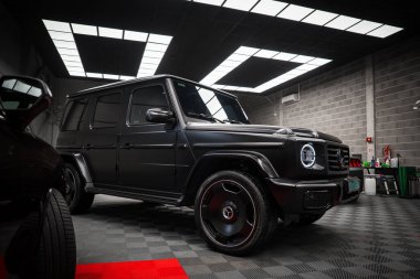 Kırmızı halı aksanlı, kapalı bir yere park edilmiş, LED farları ve parlak siyah tekerlekleri olan siyah bir Mercedes AMG sınıfı SUV..