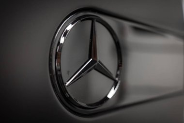 Sembolik Mercedes Benz krom çerçeveli üç köşeli yıldız logosu, ince yansımaları ve bulanık çevresi olan koyu bir arkaplan üzerine kuruludur..