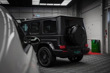 Siyah bir Mercedes AMG sınıfı SUV kapalı bir yerde kareli bir zeminde park halinde. Arka planda yedek lastik kapağı ve arka planda endüstriyel elementler var..