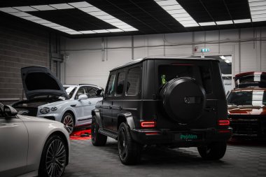 Kapalı alanda sergilenen siyah bir Mercedes AMG sınıfı SUV, kutulu arka tasarımı, yedek lastik kapağı ve stop lambaları sergileniyordu. Diğer lüks arabalar etrafını sardı..