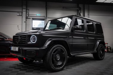 Modern bir sergi salonunun kareli zemininde dairesel LED farları ve siyah alaşımlı tekerlekleri olan siyah bir Mercedes AMG sınıfı SUV..