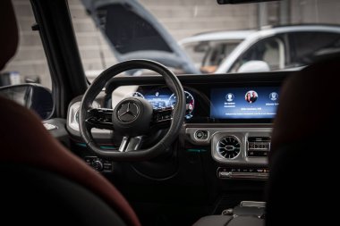 Mercedes AMG sınıfının içini kapatın. Direksiyonu, dijital gösterge panelini, metal aksanları ve arka planda bir garaj ayarını gösterin..