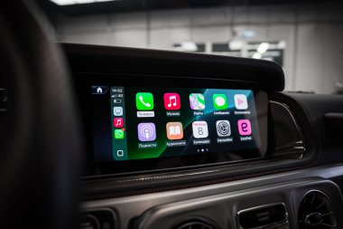 Metalik aksanlı, kırmızı dikişli deri süslemeli ve modern bir sergi salonu arka planına sahip lüks bir arabanın içindeki uygulama simgeleriyle donatılmış bir ekran..