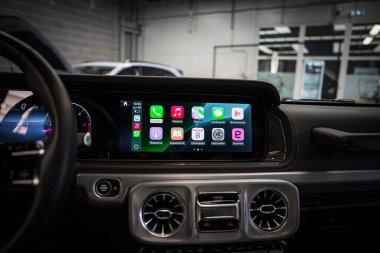Mercedes AMG 'nin iç mimarisi Apple CarPlay' i bilgi ekranında, metalik havalandırmada, kırmızı dikişli deri gösterge panelinde ve garaj ayarında gösteriyor..