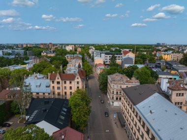 Çağdaş ve eski yapıların ufuk çizgisi ile çevreleyen yeşil ağaçlarla çevrili tarihi binalarla dolu bir Riga caddesinin havadan görünüşü.