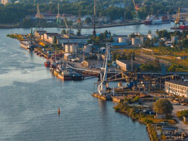 Riga, Letonya 'daki Daugava Nehri' ndeki tersanede sıcak günbatımı aydınlatması ve kentsel çevresiyle birlikte sanayi turnaları, rıhtım gemileri ve depolama tankları..