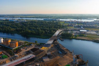 Riga, Letonya 'da bir nehir üzerinde yeni bir köprü inşaatı, turnaların, depolama tanklarının ve yeşillik ve sanayi bölgelerinin yer aldığı bir yapı..