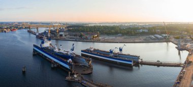 Gün batımında Riga, Letonya 'da bir tersane. Kuru rıhtımdaki iki büyük gemi vinçler, endüstriyel yapılar ve Daugava Nehri ile çevrilidir..