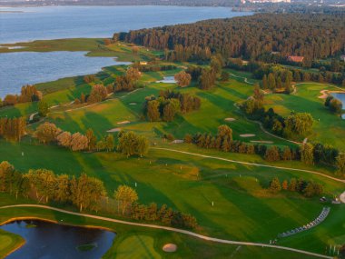 Riga yakınlarında gün batımında ormanla çevrili sakin bir nehir ya da göl yakınında yeşil golf sahası, kum sığınakları ve su tehlikeleri..