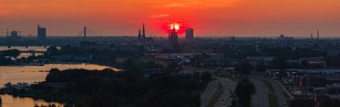 Riga, Letonya 'nın gün batımında St. Peter Kilisesi kulesi, Riga TV Kulesi, Vansu Köprüsü, Daugava Nehri, bir yol ve çevreleyen yeşillikler.