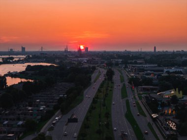 Riga, Letonya 'nın günbatımında tarihi kilise kuleleri, Riga TV Kulesi, çok şeritli bir yol, yeşillik ve ön planda Daugava Nehri yer alıyor..