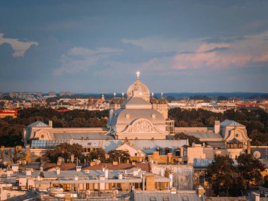 Riga, Letonya, gün batımında çatısı ve ağaçlarıyla çevrili kubbeli bir bina. Gökyüzü maviden pembeye dönüşür.