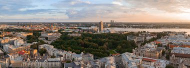Riga, Letonya 'da gün batımında Jugendstil mimarisi, bir merkez park, Daugava Nehri, Riga TV Kulesi, kilise kuleleri ve modern binalar yer alıyor..