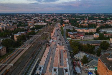 Riga, Letonya 'da tren rayları, şehir binaları, yeşillikler ve kilise kulesi ve Riga TV kulesi gibi yerleri olan bir inşaat alanının havadan görüntüsü..