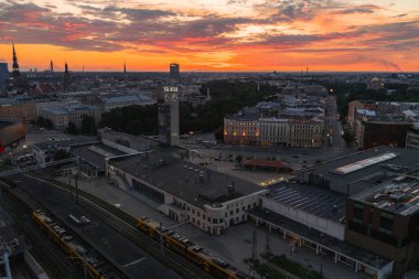 Riga, Letonya üzerinde canlı gün batımı, Riga Merkez İstasyonu, tren rayları, St. Peter Kilisesi 'nin tarihi kuleleri ve uzak yeşillikler.