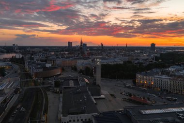 Riga, Letonya manzarası, Riga Saat Kulesi, St. Peter Kilisesi kulesi, Daugava Nehri ve günbatımı altında canlı bir gökyüzü altında modern binalar.