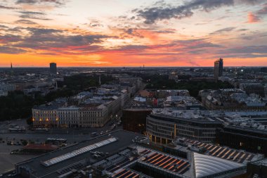 Riga, Letonya ufuk çizgisi gün batımında canlı turuncu ve pembe renklerle. Riga TV Kulesi ve kilise kulesi modern ve tarihi binaların üzerinde yükseliyor..