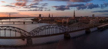 Riga, Letonya 'da gün batımında Daugava Nehri, Demiryolu Köprüsü, Riga TV Kulesi, Vansu Köprüsü ve eski kasabadaki St. Peter Kilisesi kuleleri yer alıyor..