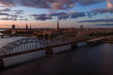 Riga, Letonya gün batımında Daugava Nehri, Demiryolu Köprüsü ve Riga Katedrali ve St. Peter Kilisesi 'nin rengarenk gökyüzü altında kuleleri..
