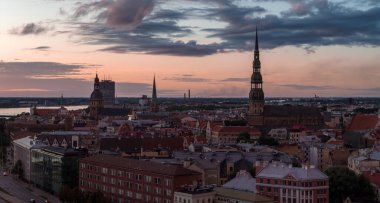 Riga 'nın eski şehir silueti gün batımında Aziz Peter Kilisesi kulesi, Riga Katedrali ve Jugendstil mimarisi ile arka planda Daugava Nehri yer almaktadır..