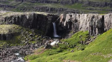 Güçlü bir şelale kayalık bir uçurumdan yemyeşil yemyeşil ve engebeli bir araziyle çevrili sakin bir havuza akar..