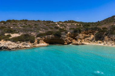 Yunanistan 'ın Girit kentindeki Voulisma Sahili' nin hava manzarasında turkuaz sular, kayalık kıyı şeridi, seyrek bitki örtüsü ve kıyı boyunca küçük bir mağara yer alıyor..