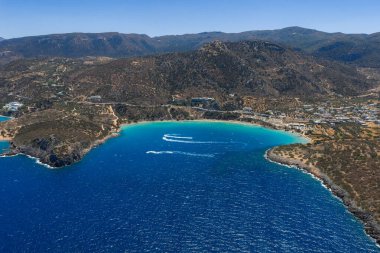 Yunanistan 'ın Girit kentindeki Voulisma Sahili' nin hava manzarasında turkuaz sular, engebeli tepeler, kıvrımlı bir körfez ve denizde beyaz tekne izleri yer alıyor..