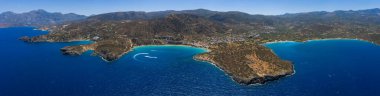 Yunanistan 'ın Girit kentindeki Voulisma Sahili' nin hava manzarasında turkuaz sular, kayalık yarımadalar, tekne yolları ve arka planda dağlık araziler yer alıyor..